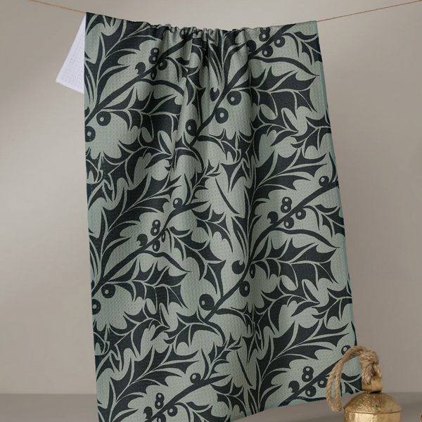 Green curtain with black leaf pattern hanging on a line against a beige wall.